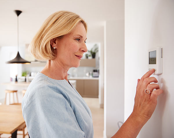 A woman adjusting the thermostat at her home.